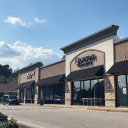 Strip mall in daylight with parked car in front.