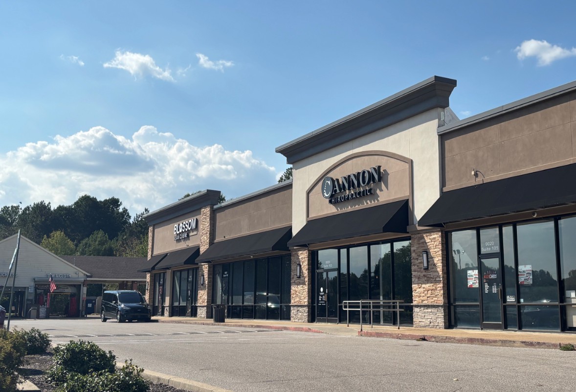 Strip mall in daylight with parked car in front.