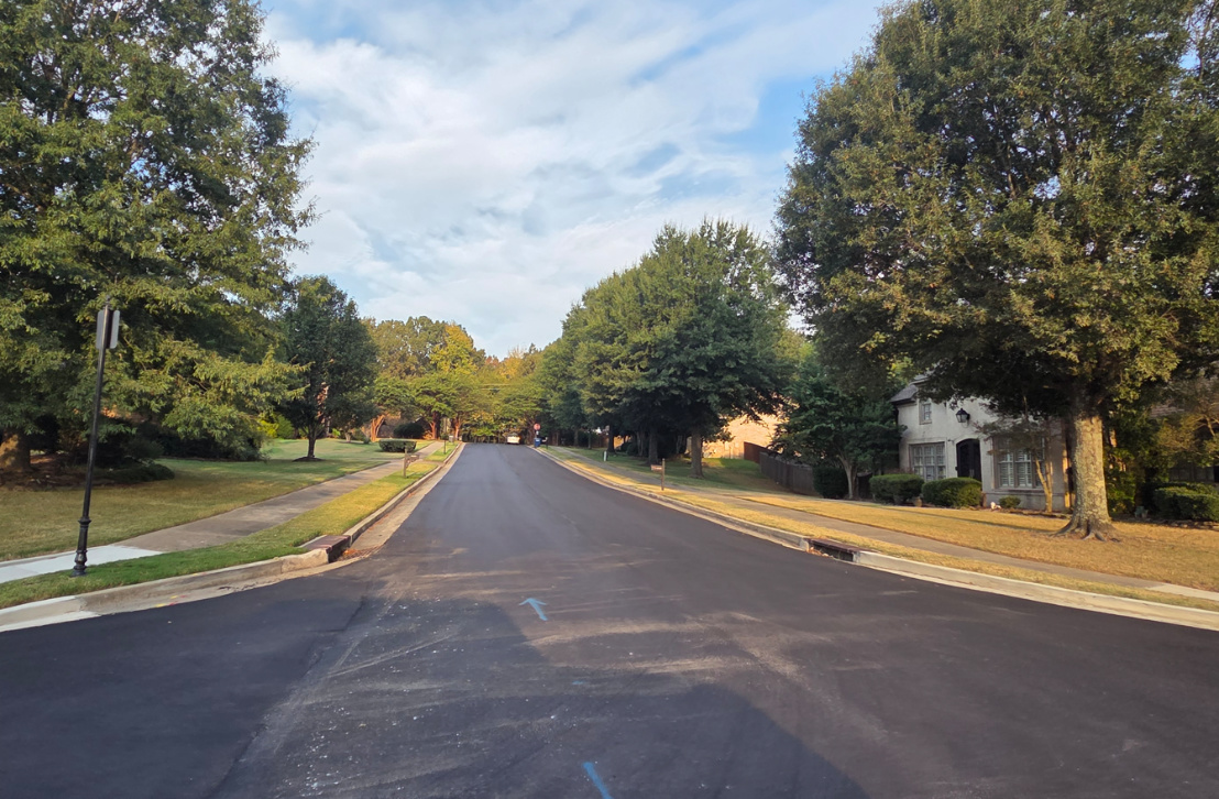 Fresh paved road on tree lined street.